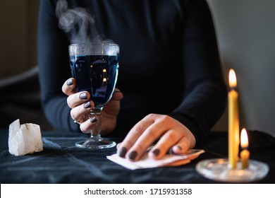 Female hands holding magic love potion and occultic fortune-telling cards on dark background.