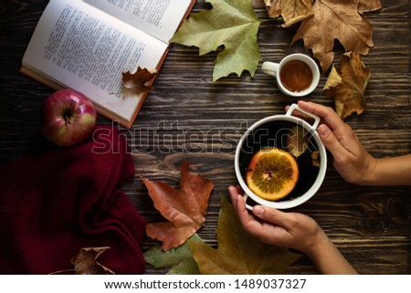 Female hands holding a mug of hot mulled wine. Mulled wine, honey, autumn leaves, apples, a book and a woolen sweater on a wooden background. Autumn cozy mood. Autumn background. Flat lay