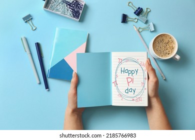 Female Hands Holding Notebook With Text HAPPY PI DAY, Cup Of Coffee And Stationery On Light Blue Background