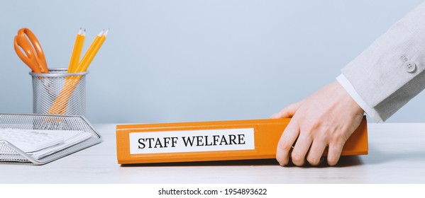 Female Hands Holding An Office Binder Folder With Staff Welfare Text On It. Welfare Guidance Or Regulations Concept