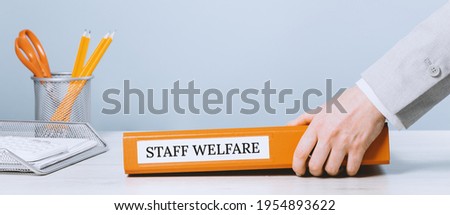 Female hands holding an office binder folder with Staff Welfare text on it. Welfare guidance or regulations concept