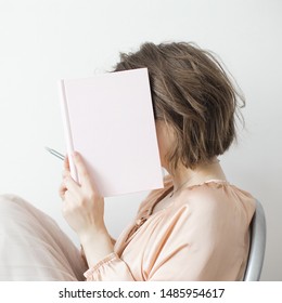 Female hands holding open book with blank cover and closing face on light background. Copy space.
