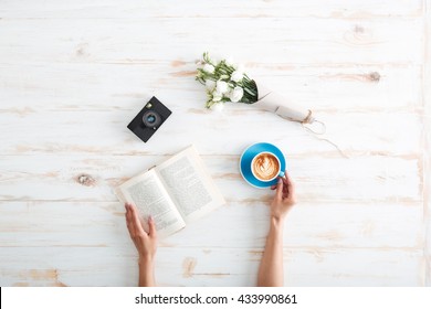 Female hands holding open book and coffee cup on the wooden desk - Powered by Shutterstock