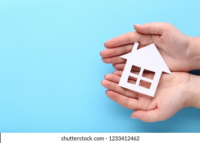 Female Hands Holding Paper House On Blue Background