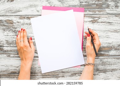 Female hands holding pen and blank paper sheets with copyspace on old wooden table. Top view