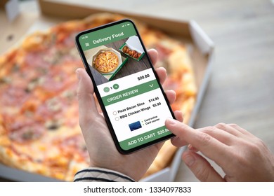 Female Hands Holding Phone With Food Delivery App On The Screen Above Pizza Box