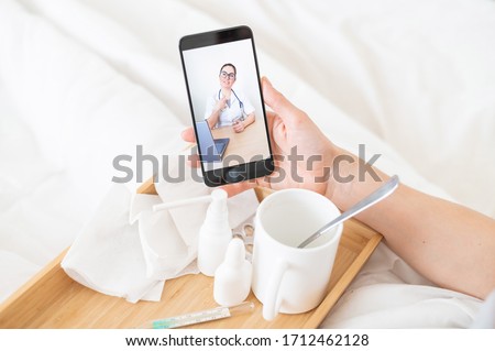 Female hands holding a phone. Remote reception at the therapist. A friendly doctor gives recommendations for treatment online. Medications and thermometer on a wooden tray.