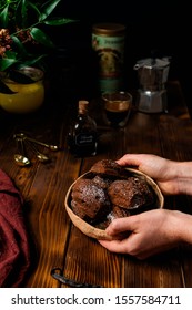 Female hands holding plate with chocolate madeleine cookies on cooling rack with ingredients and utensils, eggs, ghee butter, coffee, vanilla extract on rustic wooden background - Shutterstock ID 1557584711