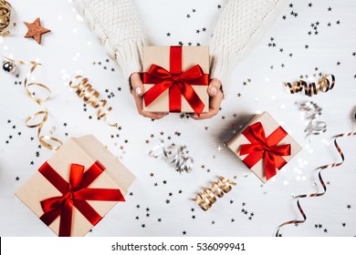 Female hands holding present with red bow on white rustic sparkling background. Festive backdrop for holidays: Birthday, Valentines day, Christmas, New Year. Flat lay style