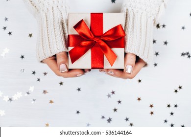 Female hands holding present with red bow on white rustic sparkling background. Festive backdrop for holidays: Birthday, Valentines day, Christmas, New Year. Flat lay style - Shutterstock ID 536144164