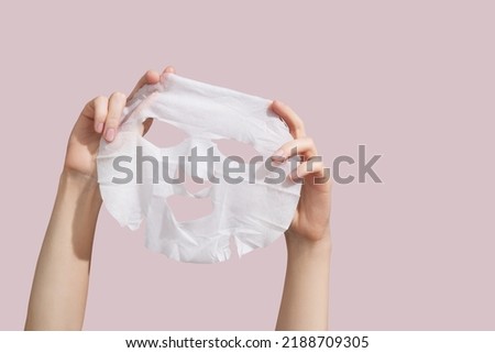 Female hands holding sheet of white mask on pink background. High quality photo