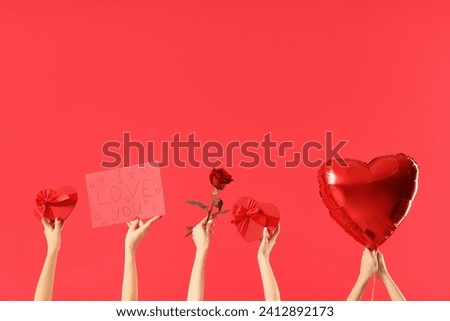 Female hands holding sign with text I LOVE YOU and heart-shaped gift boxes, balloon and rose on red background. Valentine's Day celebration