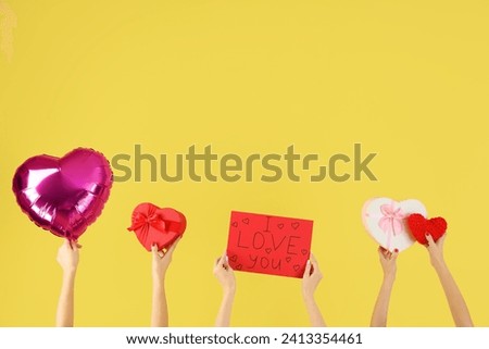 Female hands holding sign with text I LOVE YOU, heart-shaped gift boxes and balloon on yellow background. Valentine's Day celebration