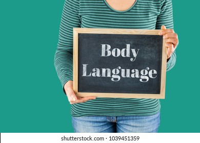 Female Hands Holding Small Black Chalkboard In Front Of The Body With Written Words Saying Body Language