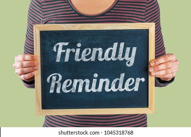 Female hands holding small black chalkboard in front of the body with written words saying Friendly Reminder