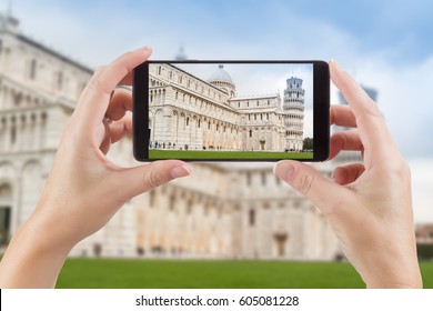 Female Hands Holding Smart Phone Displaying Photo Of The Leaning Tower Of Pisa Behind.