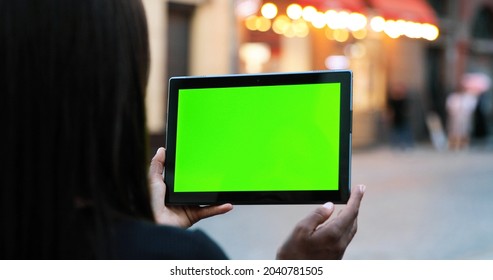 Female Hands Holding Tablet With Green Screen. Girl Using Mobile Phone While Walking In The Autumn Street. Back View Shot. Chroma Key, Close Up Woman Hand Holding Device With Vertical Green Screen 