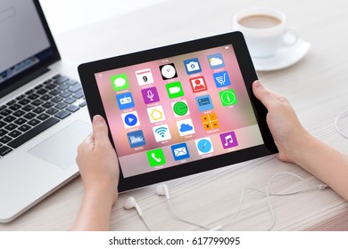 female hands holding tablet with home screen icons apps background laptop and headphones