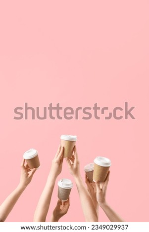 Female hands holding takeaway cups of coffee on pink background