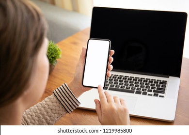 Female Hands Holding Touch Phone With Isolated Screen Above The Table With Laptop In The Office