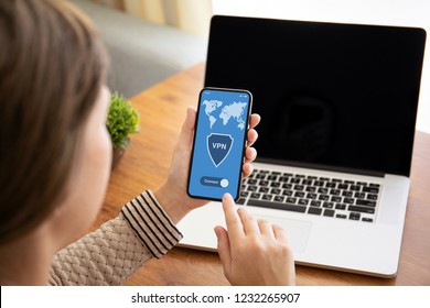 female hands holding touch phone with app vpn on screen above the table with laptop in the office