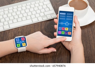 Female hands holding touch phone and smart watch with app smart home on screen 