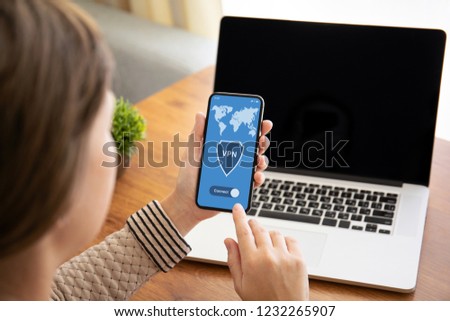female hands holding touch phone with app vpn on screen above the table with laptop in the office