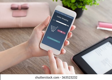 Female Hands Holding White Phone With Online Shopping On The Screen And E-rider On The Women Table