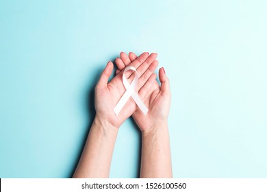 Female Hands Holding White Ribbon On A Blue Background. November Lung Cancer Awareness Month.