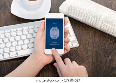 female hands holding a white touch phone over the desk in the office and entering the PIN code of fingerprint 
