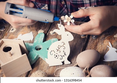 Female Hands Holding Wooden Easter Bunny And Hot Glue Gun, DIY Composition On Rustic Wooden Table