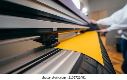 Female hands holding yellow printable material on alarge format printing plotter. Graphic design and  advertising concept.