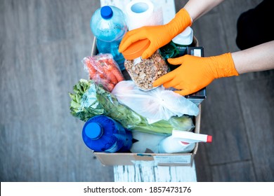 Female Hands In Hygenic Gloves  Packing Humanitarian Aid In Donation Box. Volunteer Loading Food In Charitable Foundation. Helping In Crises And Homeless 