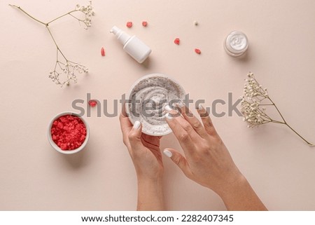 Female hands with jar of body scrub, cosmetic products, sea salt and gypsophila flowers on color background
