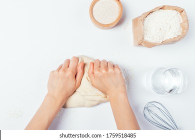 Female Hands Kneading Dough On White Table Next To Ingredients And Utensils, Top View.