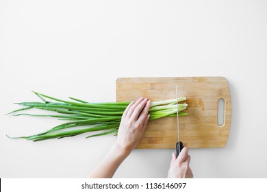 Female Hands With A Knife, Slicing Vegetables On A Wooden Board On A White Background.