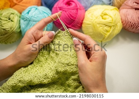 female hands knit a pullover, scarf or shawl with knitting needles from green yarn.