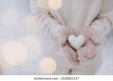 Female hands in knitted mittens hold a snow heart on a winter background - Powered by Shutterstock