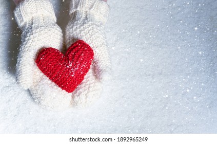 Female Hands In Knitted Mittens With Red Heart Against Snow Background. Love, Winter And Valentines Day Romantic Creative Concept With Copy Space For Text