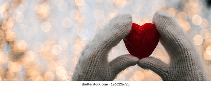 Female Hands In Knitted White Mittens With Heart Of Snow In Winter Day. Love And St. Valentine Cozy Concept, Copyspace, Bokeh Background, Banner