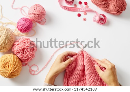 Female hands knitting with pink wool, on a white background, top view