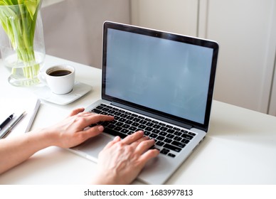 Female hands with laptop computer white blank screen on work table front view. Home office concept. Female office desk workspace homeoffice mock up with laptop, white tulips, smartphone and coffe