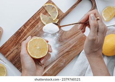 female hands with a lemon in one and a golden spoon with soda in the other clean a wooden cutting board.lemons, and a linen towel - Powered by Shutterstock