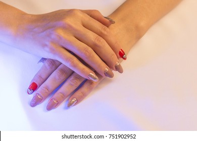 Female Hands Lie On Top Of Each Other, Showing A Beautiful Handmade Art Manicure On A Light Fabric Background. Heart On A Red Nail. Close-up.