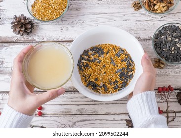 Female Hands Make Bird Food For The Winter. Seeds, Millet, Nuts, Ghee In A Bowl For Making A Feeder On A Wooden White Background