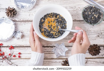 Female Hands Make Bird Food For The Winter. Seeds, Millet, Nuts, Ghee In A Bowl For Making A Feeder On A Wooden White Background