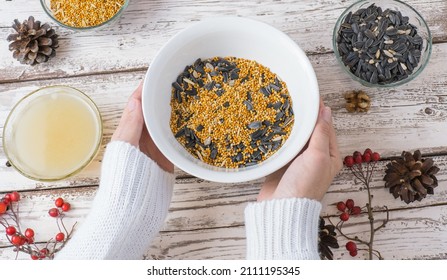 Female Hands Make Bird Food For The Winter. Seeds, Millet, Nuts, Ghee In A Bowl For Making A Feeder On A Wooden White Background