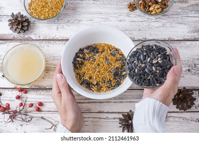 Female Hands Make Bird Food For The Winter. Seeds, Millet, Nuts, Ghee In A Bowl For Making A Feeder On A Wooden White Background