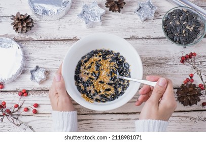 Female Hands Make Bird Food For The Winter. Seeds, Millet, Nuts, Ghee In A Bowl For Making A Feeder On A Wooden White Background