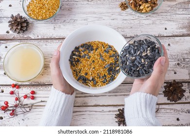 Female Hands Make Bird Food For The Winter. Seeds, Millet, Nuts, Ghee In A Bowl For Making A Feeder On A Wooden White Background